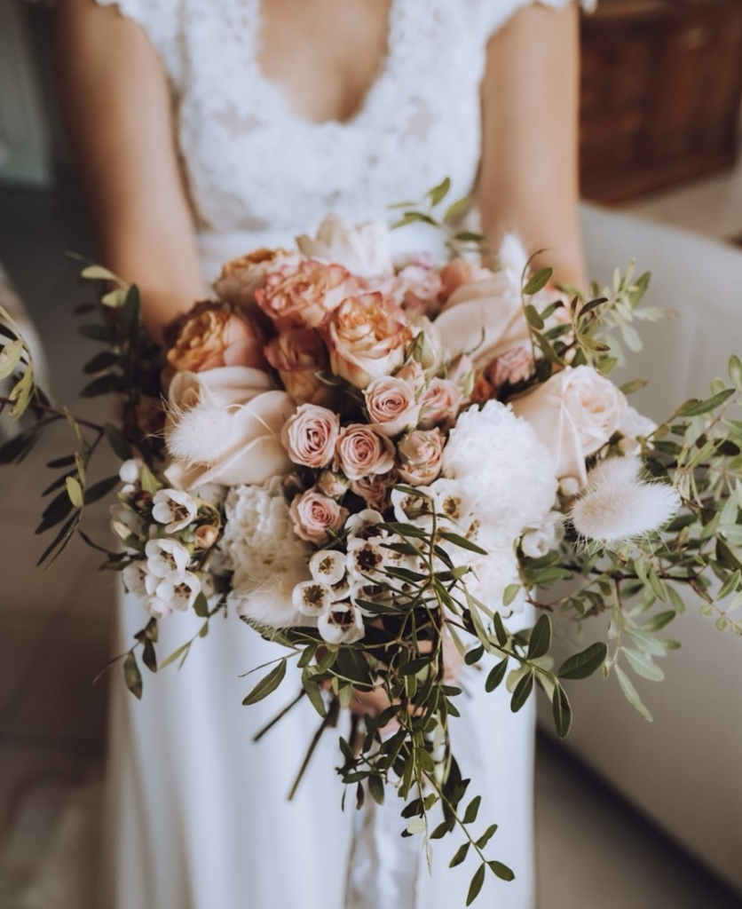 Mariée en robe blanche tenant un bouquet de roses pêche, pivoines et eucalyptus