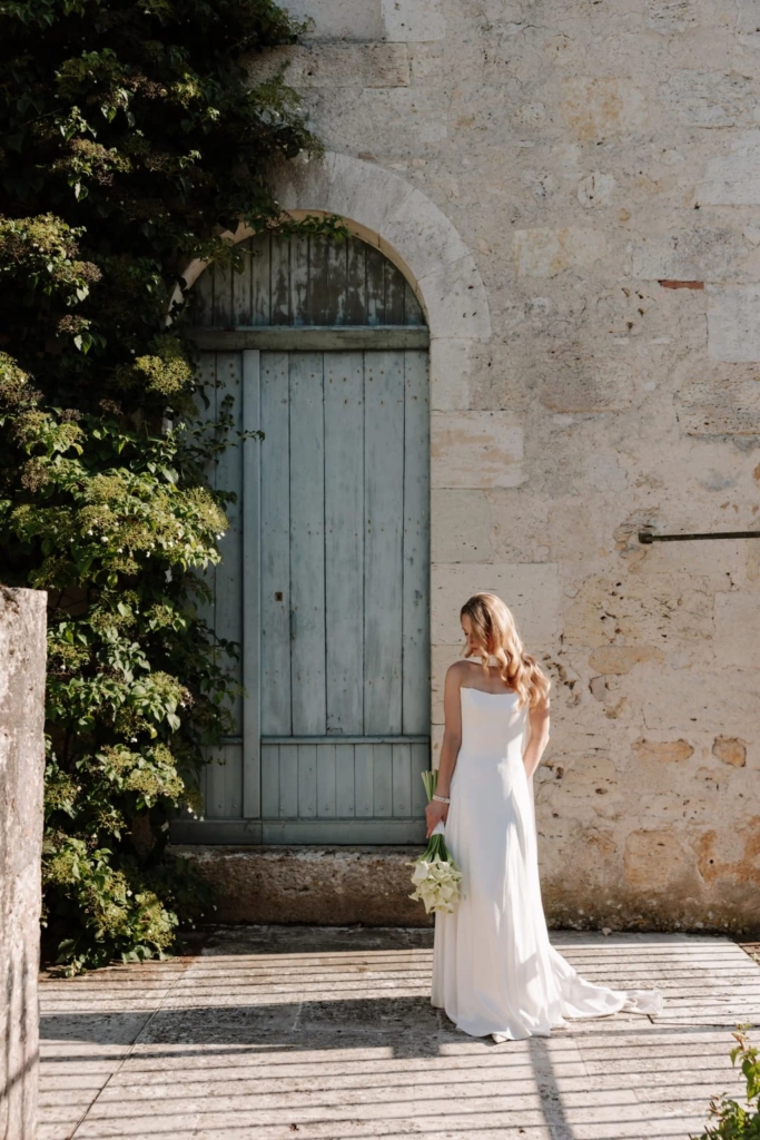 Bride in white gown holding white bouquet in chateau courtyard with stone walls and ivy