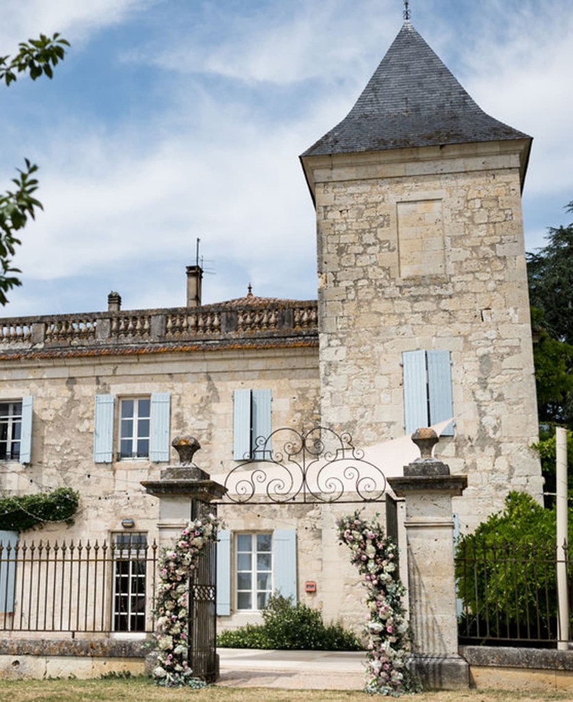 Elegant stone chateau with tower and ornate gate framed by lush greenery, typical French wedding venue setting.