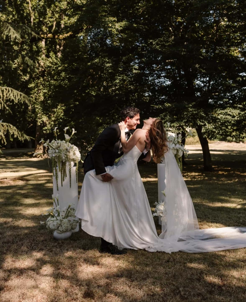 Groom dipping the bride for a kiss in a park with white floral urns
