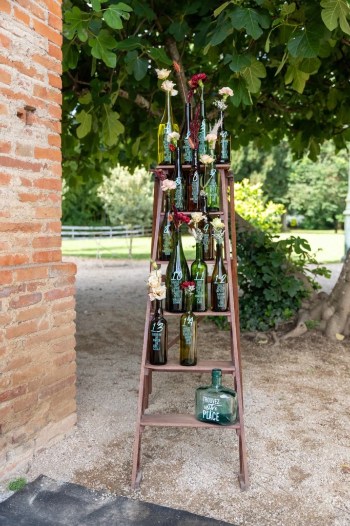 Échelle en bois avec bouteilles de vin et fleurs roses et blanches pour mariage en domaine.
